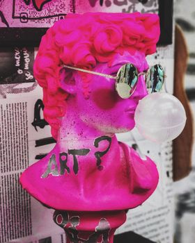 Colorful statue with sunglasses and bubblegum posing the question 'Art?' on vibrant background.