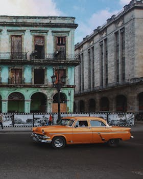 A classic orange car drives past colorful historic buildings on Havana's streets.