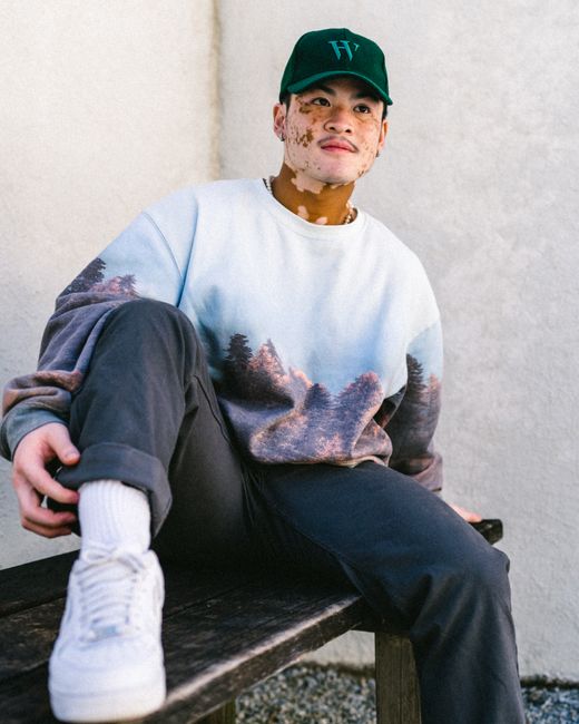 A young man in casual streetwear sits on a bench outdoors, exuding a cool fashion vibe.