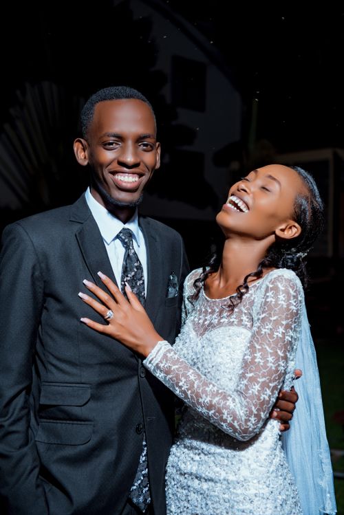 Free Laughing newlyweds posing in elegant wedding attire against a dark background. Stock Photo