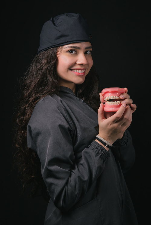 Free Smiling young female dentist with curly hair holding a dental model in a studio. Stock Photo