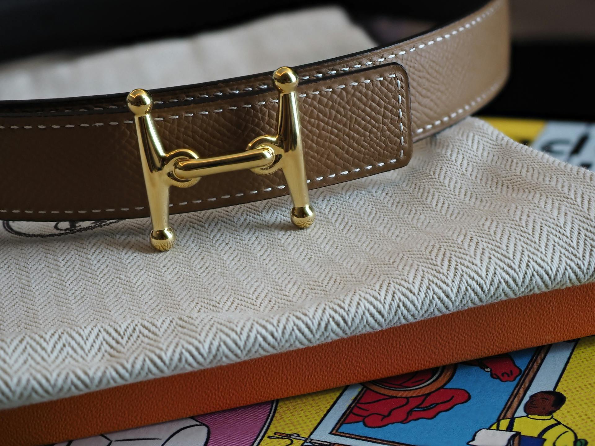 Close-up of a luxury leather belt with a golden buckle on fabric, perfect for fashion enthusiasts.