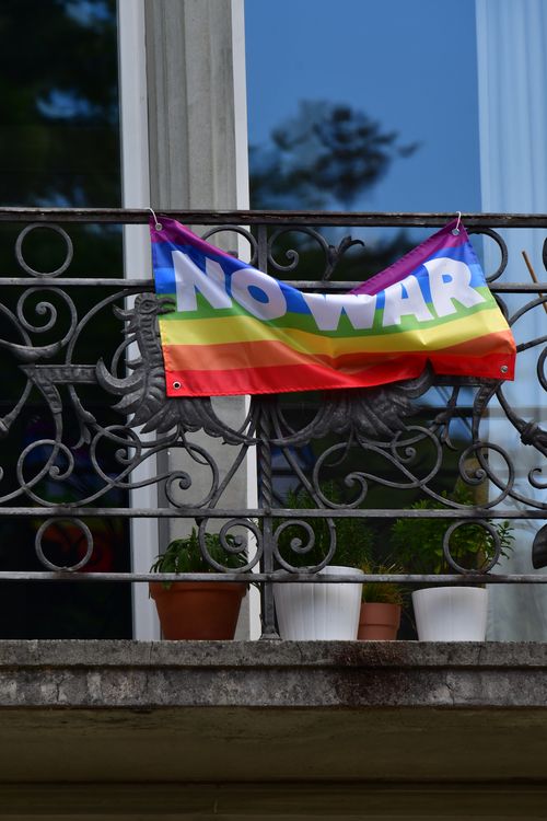 Free A colorful 'no war' banner hangs on an iron balcony with potted plants, symbolizing peace. Stock Photo