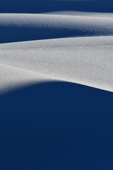 Elegant layers of sparkling snow dunes under soft winter sunlight, capturing serene nature beauty.