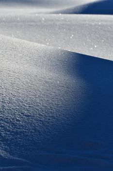 Serene snow-covered hills glisten under sunlight, capturing winter's beauty with soft shadows.