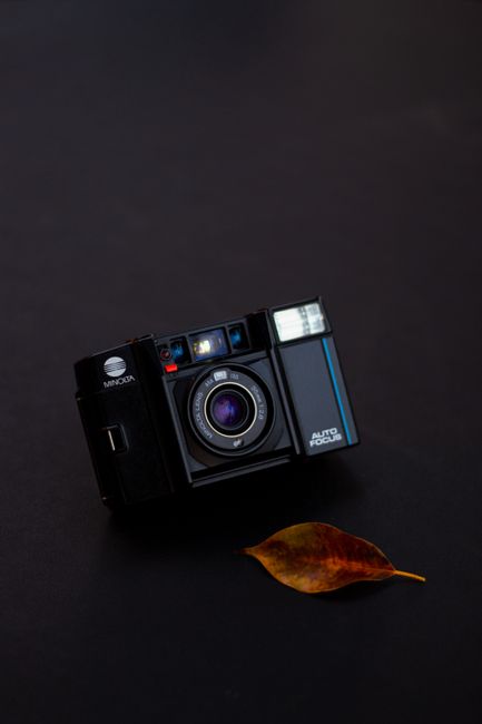 A classic film camera paired with a fallen leaf on a black surface, highlighting nostalgia in photography.
