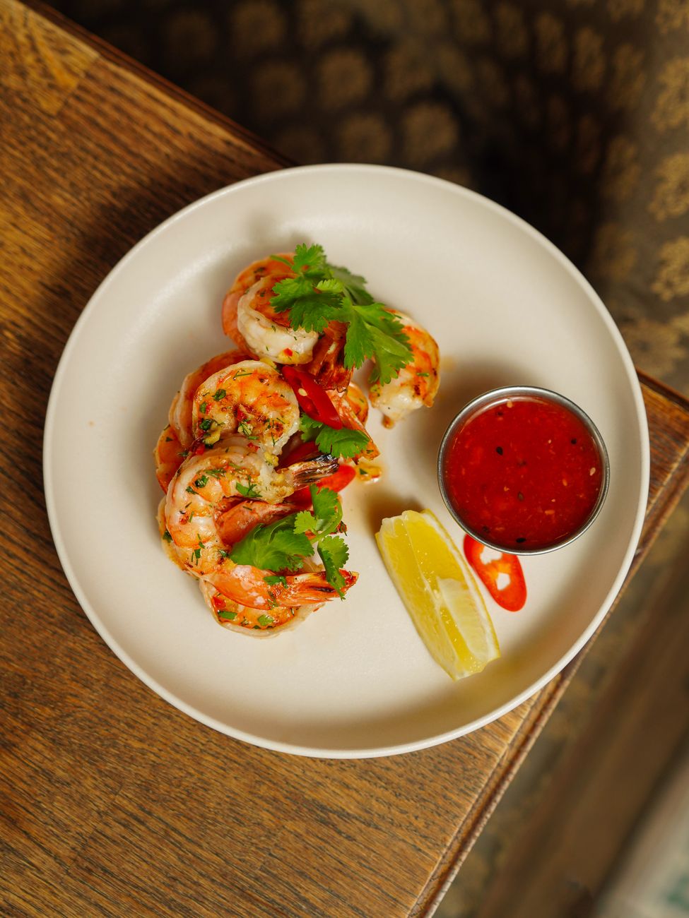 Large pink shrimp covered in deep red devil's sauce, garnished with chopped cilantro and served on a white plate
