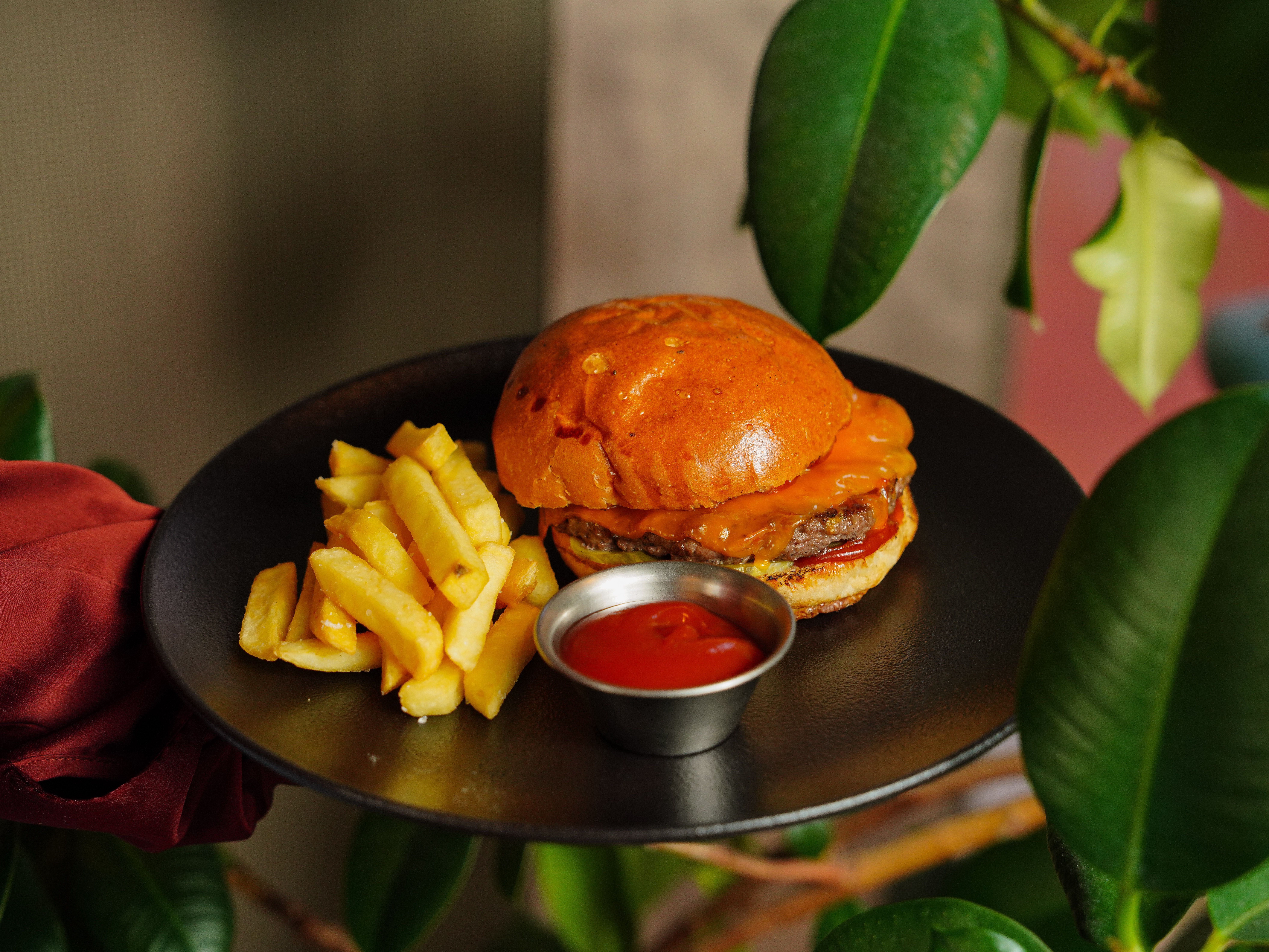 Close-up of a juicy burger with crispy fries and ketchup served on a black plate.