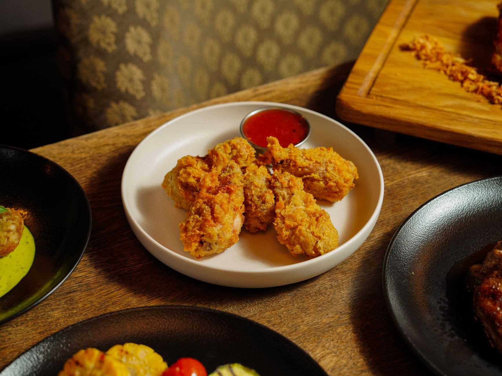 Plate of crispy fried chicken served with dipping sauce on a wooden table.