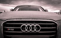 阴云密布的天空下，一辆奥迪汽车的前格栅被雨水覆盖，特写镜头展现出它的豪华与优雅