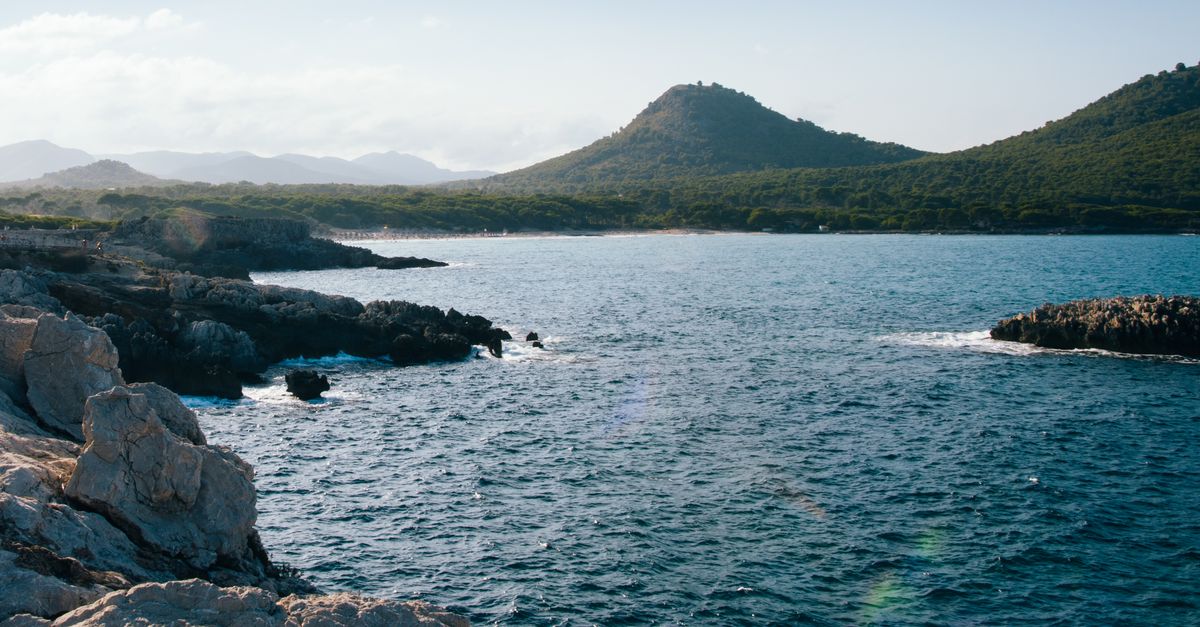 Stunning coastal view with rocky shores and mountains in Mallorca under a clear blue sky.