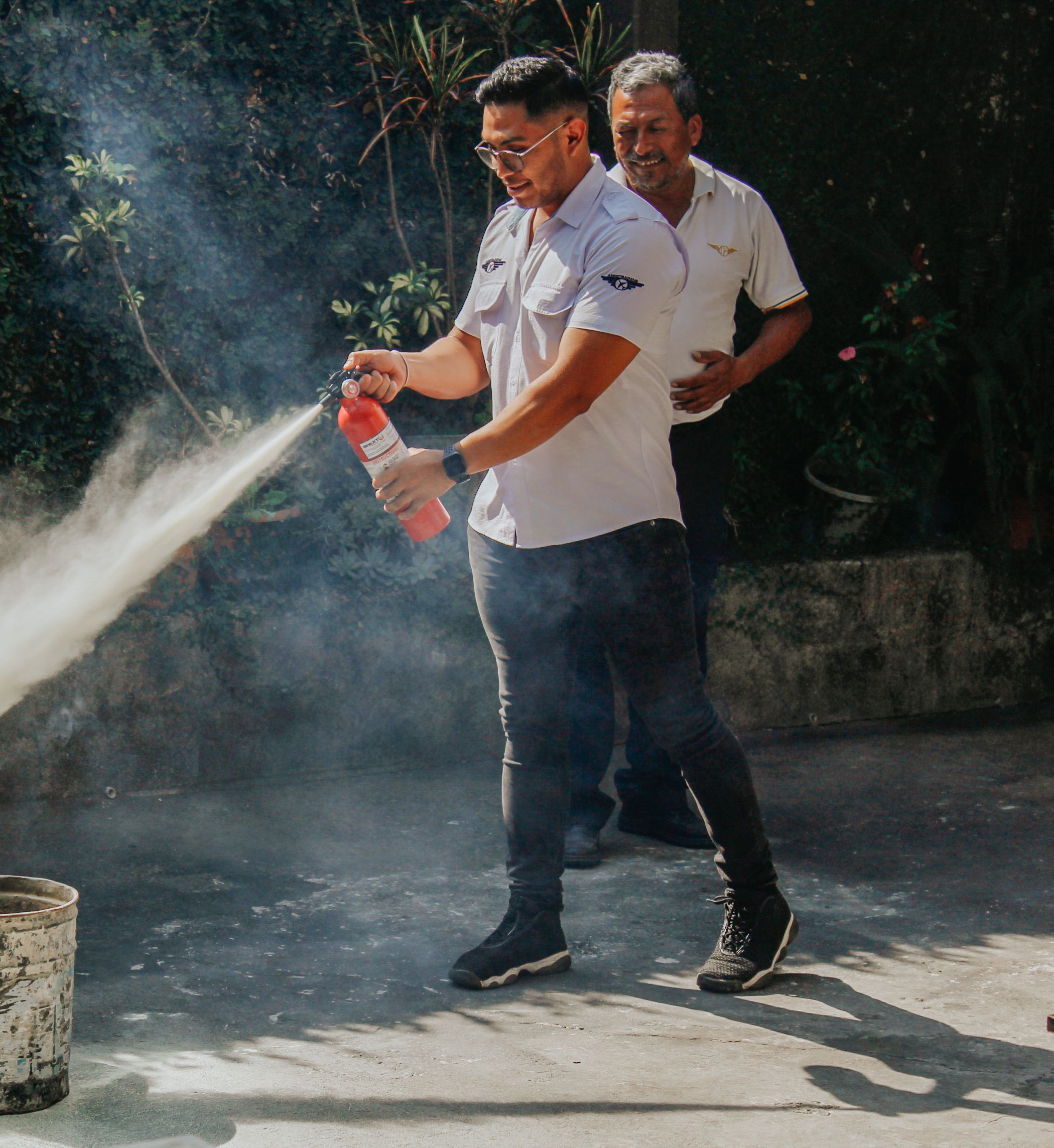 An adult practicing fire extinguisher use during an outdoor training exercise