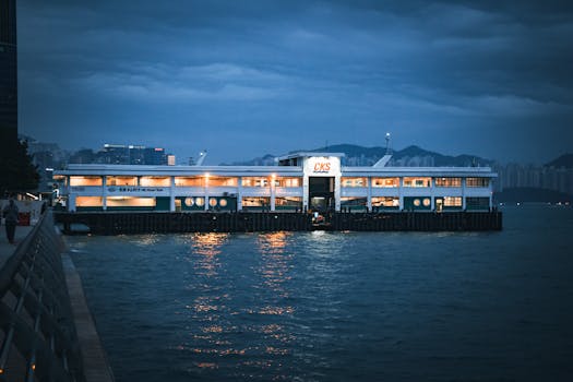 A beautifully illuminated ferry pier against a cloudy night sky, reflecting on calm waters.