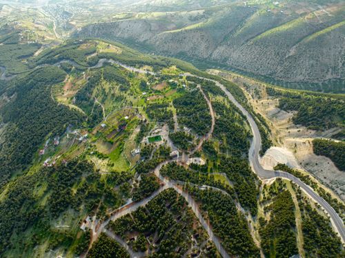 Free Scenic aerial landscape of green hills and winding roads under a summer sky. Stock Photo