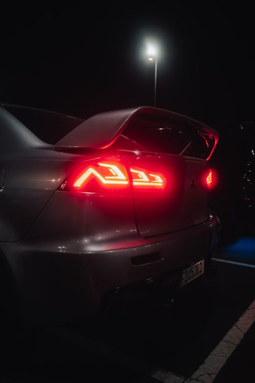 Free Stunning rear view of a sleek sports car with glowing red taillights and a prominent spoiler at night. Stock Photo