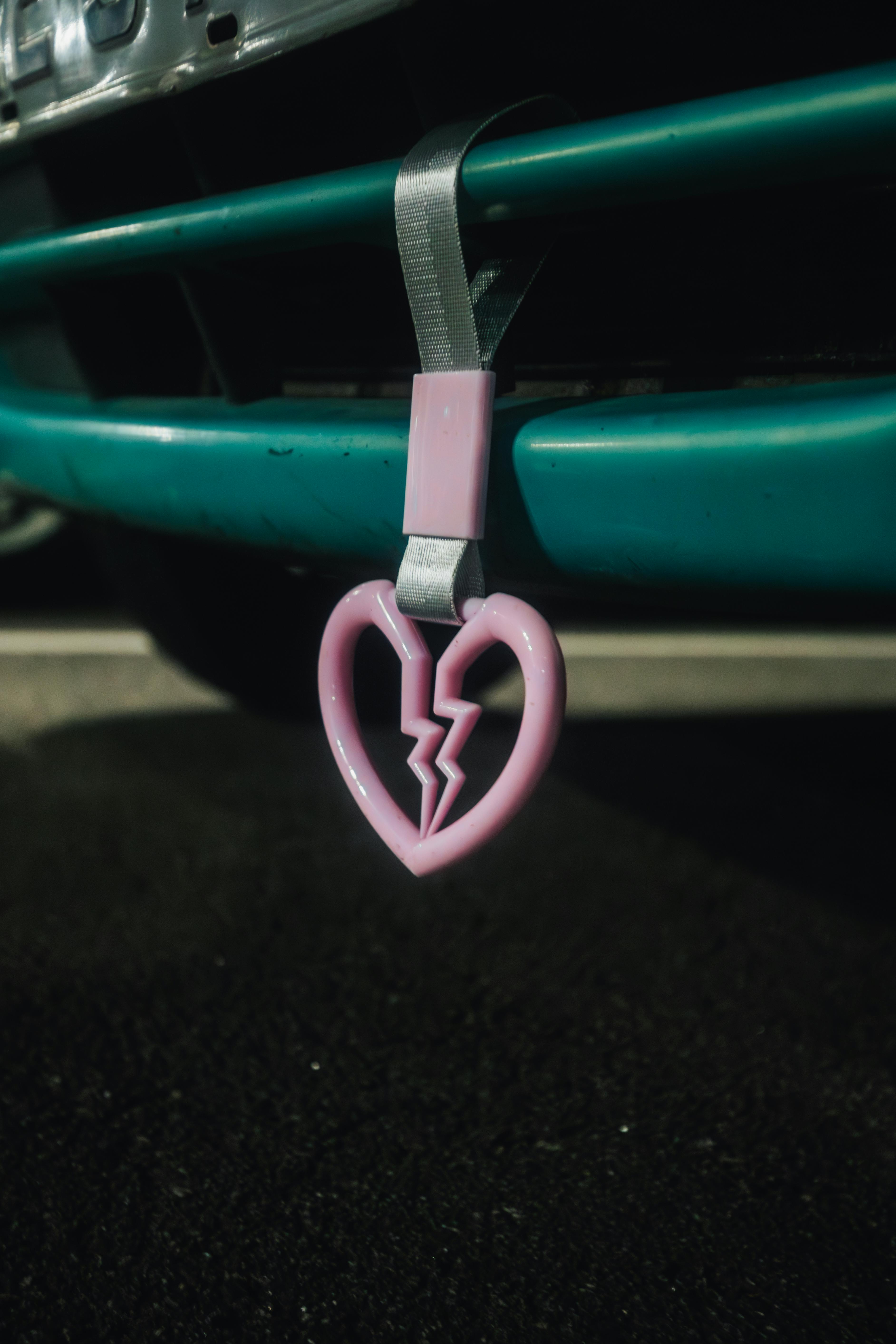 A captivating close-up of a pink heart-shaped tsurikawa hanging from a car bumper.
