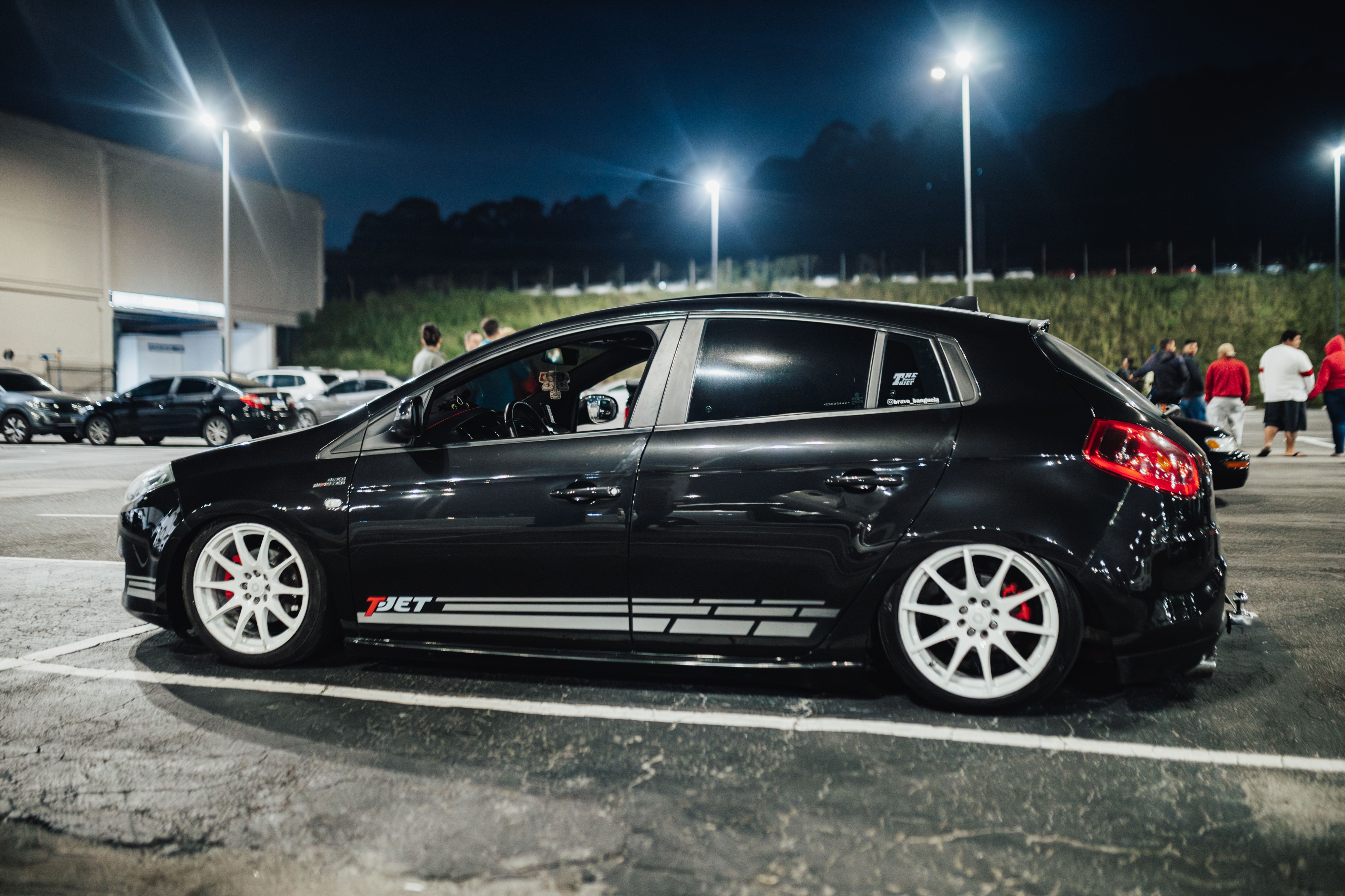 Stylish black hatchback car parked under lights in a night parking lot.