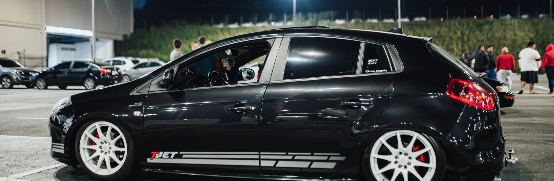 Stylish black hatchback car parked under lights in a night parking lot.