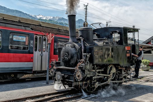 Vintage steam locomotive at Austrian station with conductor, scenic mountain view.