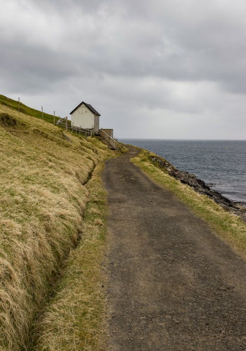 View of a Dirt Road and a House on a Shore under a Cloudy Sky 