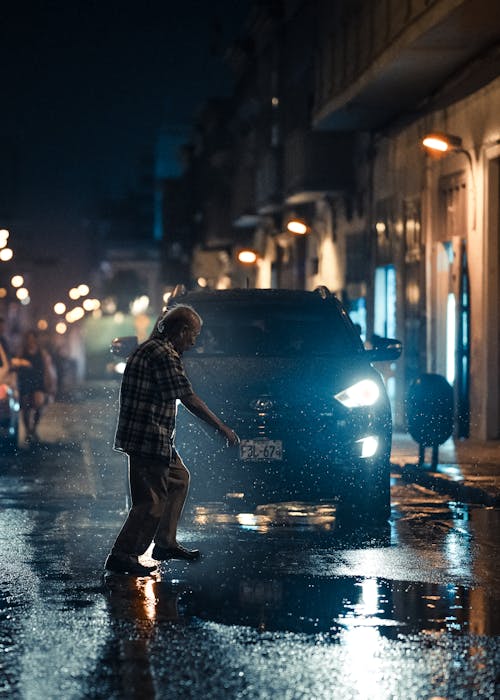 Man Crossing the Street in Front of a Car on a Rainy Night 