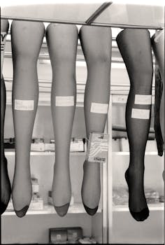 Black and white image of stockings on mannequins in a storefront window display.