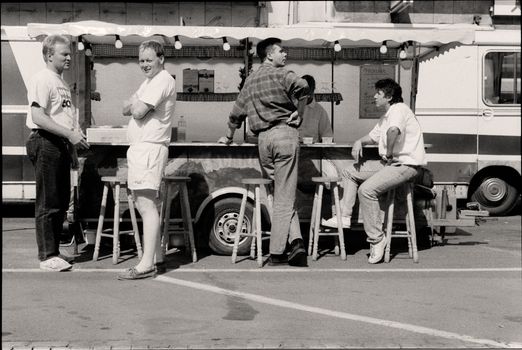 Black and white photo of men at a food stand, capturing a relaxed urban moment.