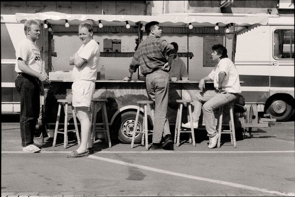Black and white photo of men at a food stand, capturing a relaxed urban moment.
