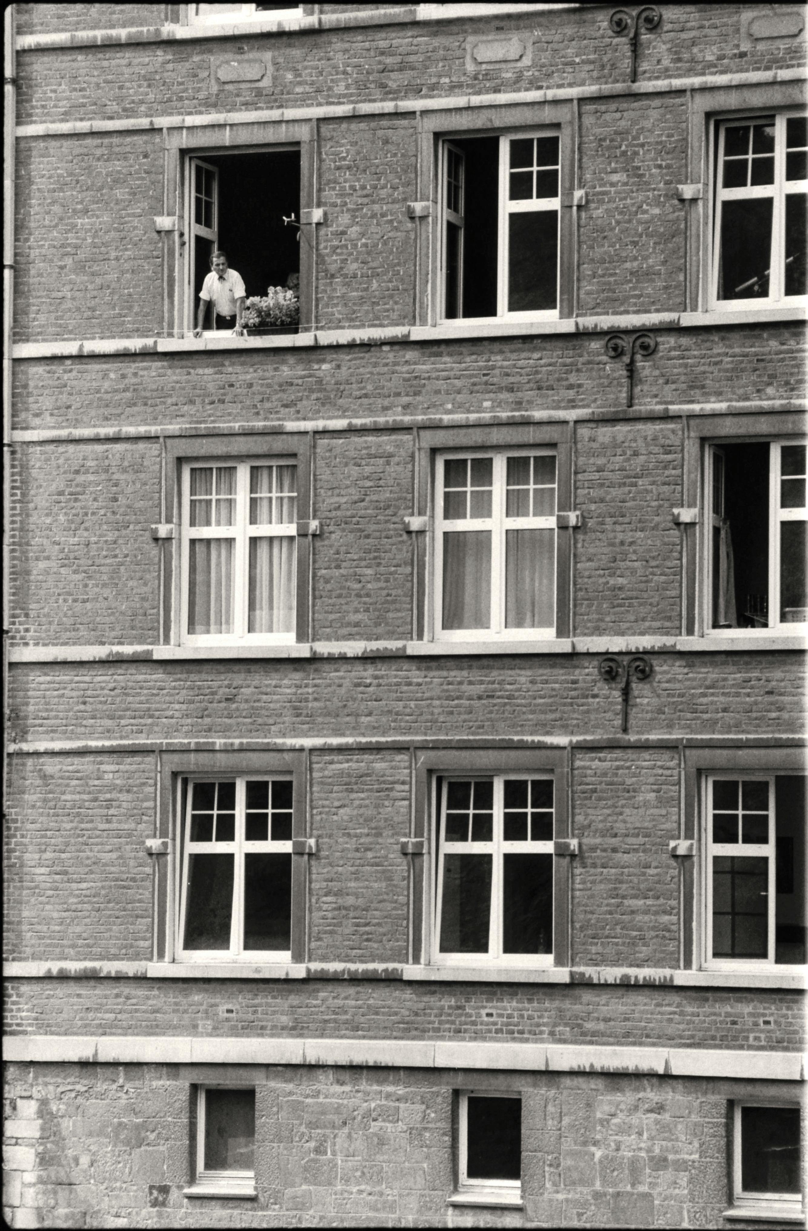 Monochrome shot of a brick building facade with multiple windows and a person at one window.