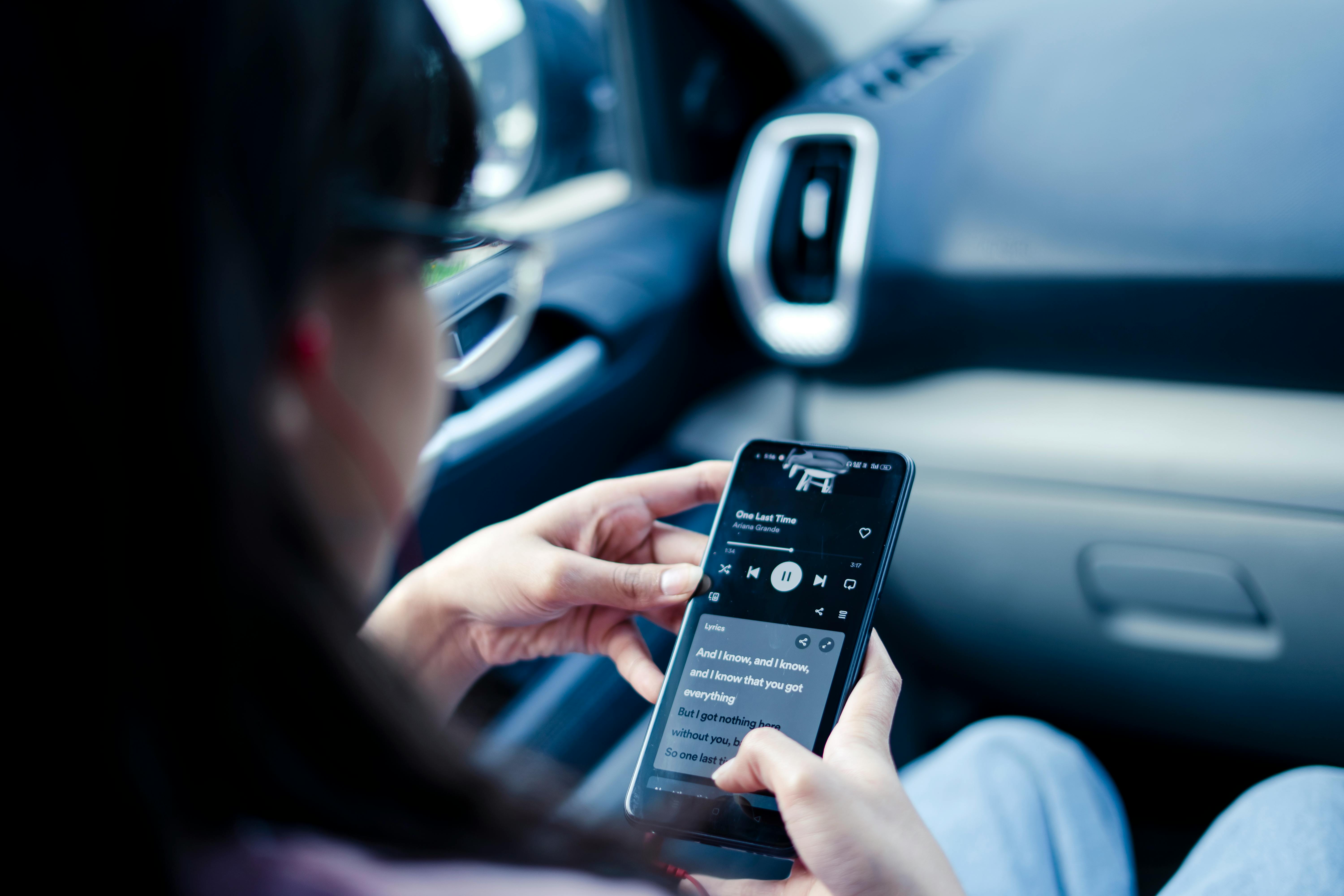 a girl sitting in a car listening to music on her smartphone and looking at song lyrics