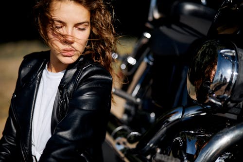 Woman in a Leather Jacket Sitting next to a Motorcycle 