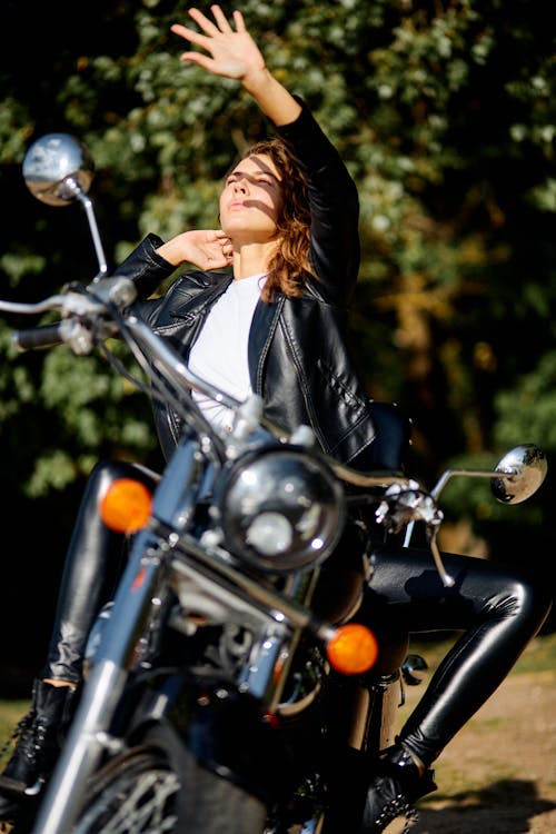 Woman Sitting on a Motorcycle and Raising Her Hand 