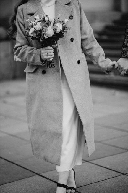 Black and white photo of a woman in a coat holding a bouquet, walking hand in hand.