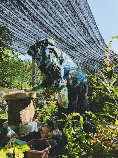 Man in Protective Clothing Standing next to a Beehive 