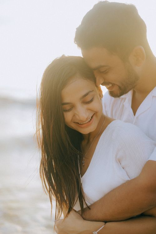 Free A romantic couple sharing a tender moment on the beach during sunset. Stock Photo