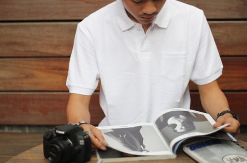 無料 黒キヤノンデジタル一眼レフカメラの横にある雑誌を読む男 写真素材