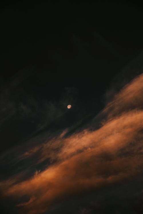 The moon is seen through clouds in a dark sky