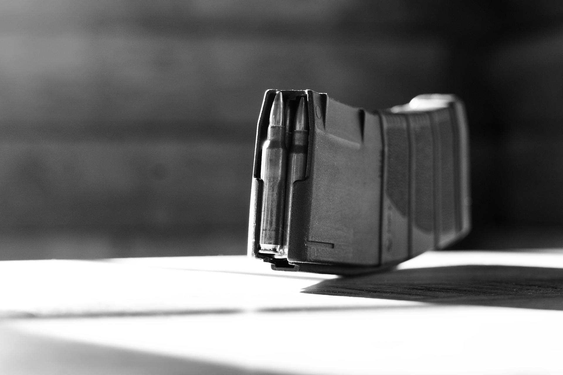 Black and white close-up of a firearm magazine with visible ammunition, emphasizing detail.