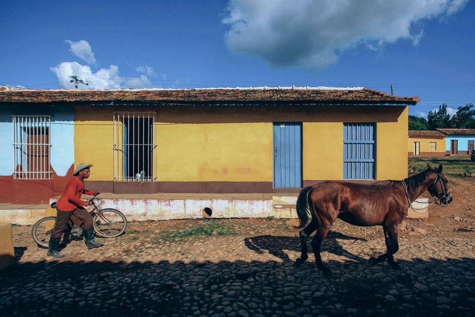 A rustic scene of a man with a bike leading a horse by colorful houses in a rural setting.