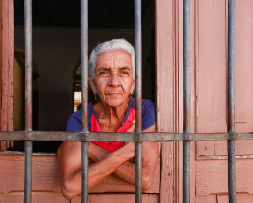 Free Senior woman looking through barred window, evoking resilience and introspection. Stock Photo