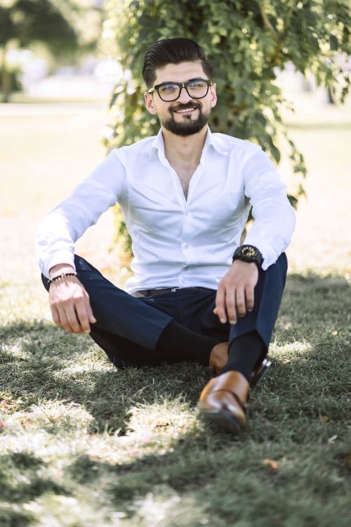 Free A fashionable man sitting on grass in a park, exuding a relaxed demeanor. Stock Photo