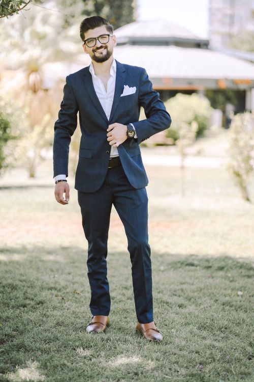 Free Confident man in a navy suit with glasses smiling outdoors in a park. Stock Photo