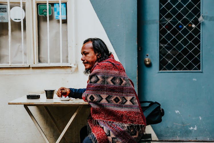 A Man Sitting At The Table Outside Of A Building And Drinking Tea 