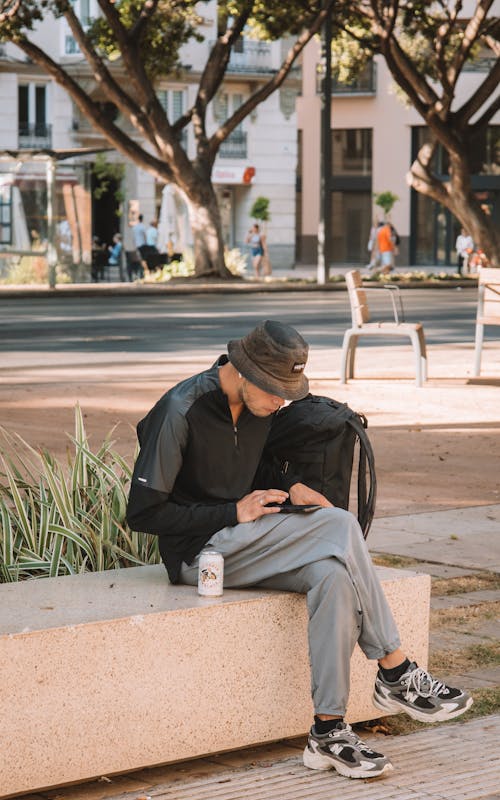 Man in Hat Sitting with Smartphone on Bench