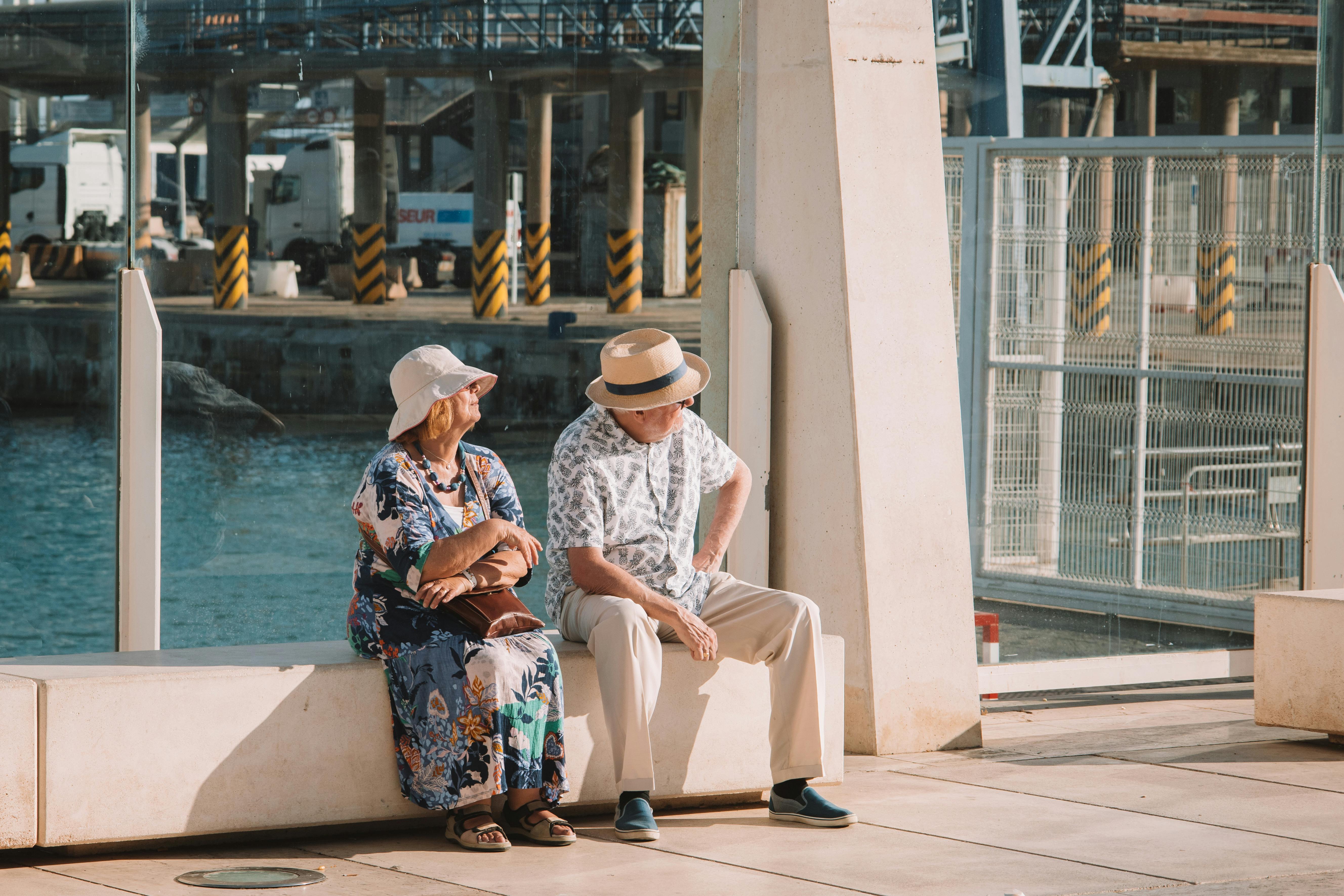 Senior couple seated outdoors in Málaga, Spain enjoying a sunny day by the waterfront.