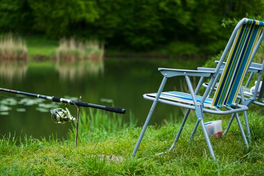 Relax by the lakeside with this inviting fishing setup and striped chairs for a perfect summer day.
