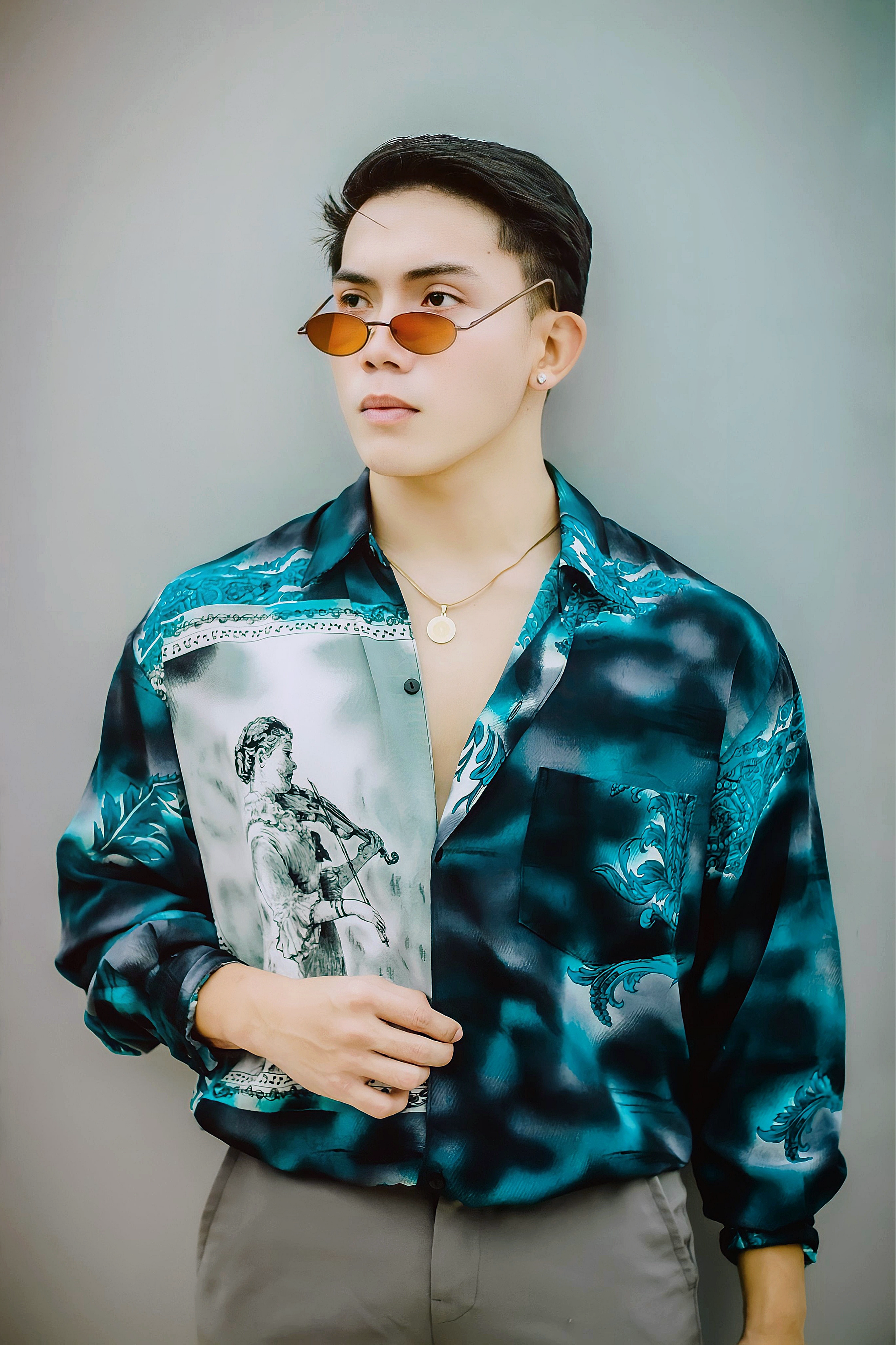 Fashionable young man in a stylish shirt and sunglasses posing confidently indoors.