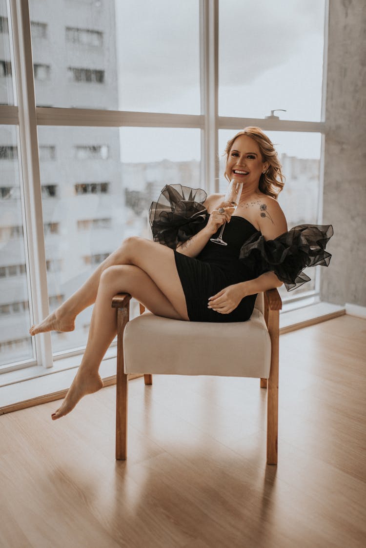 Woman In A Black Dress Holding A Glass Of Champagne And Sitting In Chair 