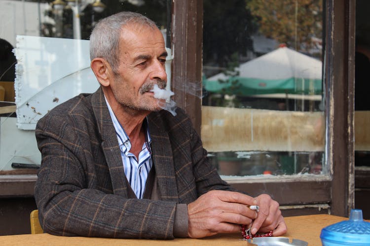 Old Man Sitting At Cafe Table Smoking