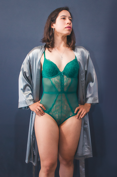 Woman posing in elegant green lingerie and silk robe, exuding confidence in a studio setting.